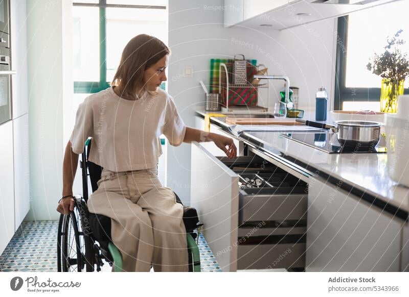 Young woman on wheelchair doing house chores in modern kitchen home housework domestic household apartment busy casual lifestyle disable young female
