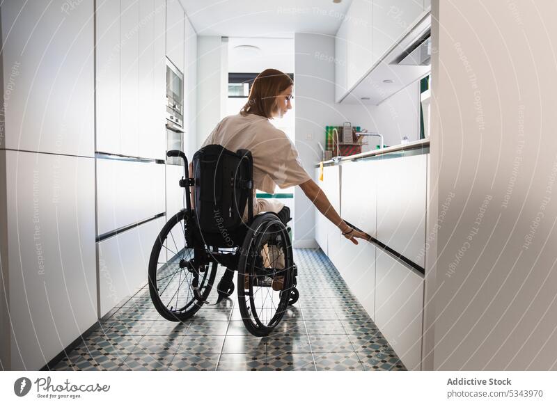 Young disabled woman on wheelchair beside opened cupboard in kitchen fridge handicap at home apartment casual hungry young female daylight domestic lifestyle