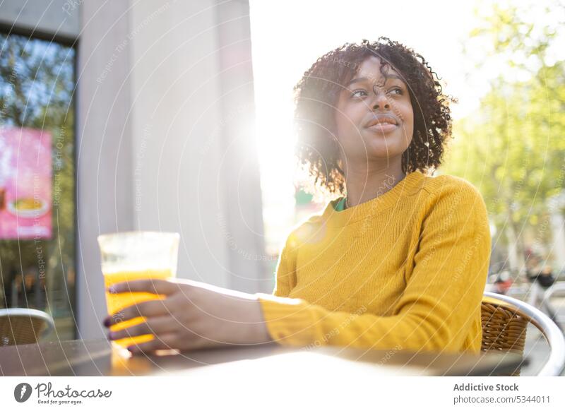 Happy black woman sitting with glass of orange juice smile positive enjoy glad pleasant cafe cheerful drink happy female young curly hair african american