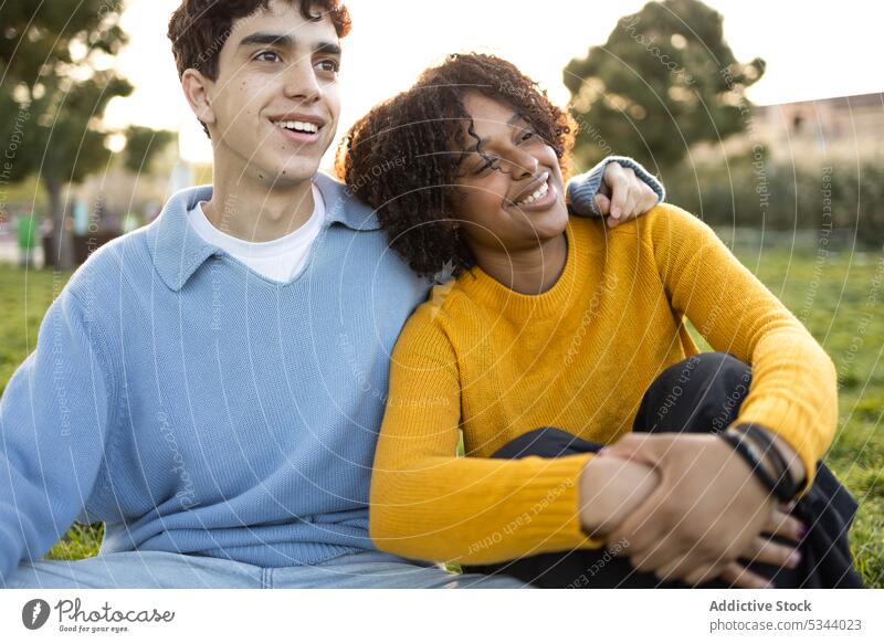 Cheerful friends looking away sitting on grass in park man woman lying friendship smile relax daylight daytime multiracial diverse multiethnic nature lawn