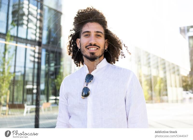 Happy ethnic man standing on street and looking at camera positive smile style city outfit trendy curly hair happy optimist toothy smile individuality black