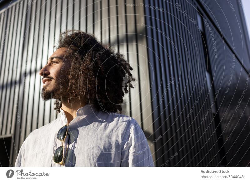 Happy ethnic man with curly hair looking away street confident city pensive afro gadget male african american black modern casual style using urban device