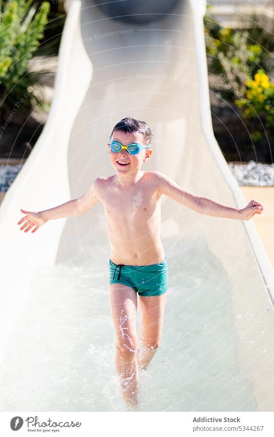 Happy boy running on water slide thumb up gesture smile resort vacation happy summer swimwear cheerful goggles kid holiday child approve trip recreation