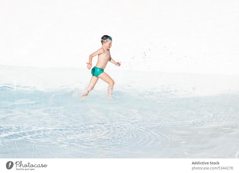 Happy boy running in swimming pool with water summer vacation resort holiday splash transparent kid shirtless poolside child recreation activity active tropical