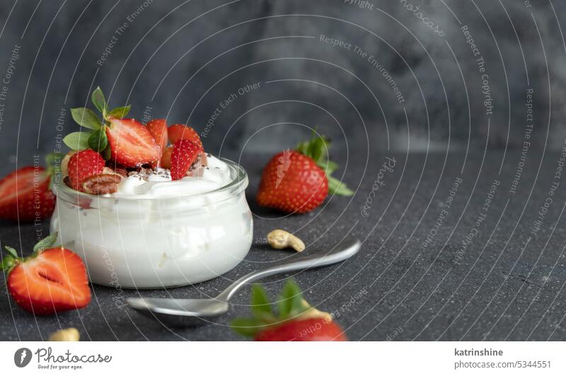 Glass jar of Greek yogurt, nuts and strawberries on grey table with a spoon close up, copy space breakfast Healthy fruits eat protein glass concrete red food
