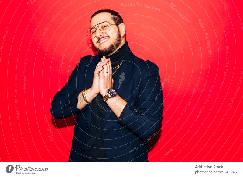 Rich, cheerful man, hands clasped together, in a red studio portrait rich mafia luxury confident self assured fashion outfit suit smiling young entrepreneur