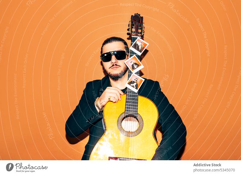 Emotionless man with acoustic guitar in studio hipster style musician guitarist trendy sunglasses male beard individuality confident serious hobby calm