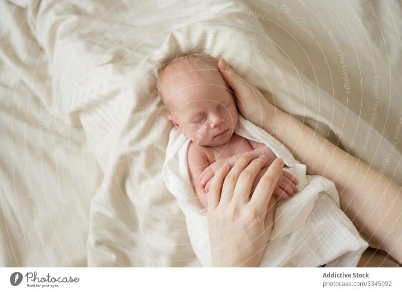 Anonymous mother stroking infant on soft bed baby newborn sleep mom stroke caress vulnerable child innocent comfort cozy peaceful lying blanket asleep rest