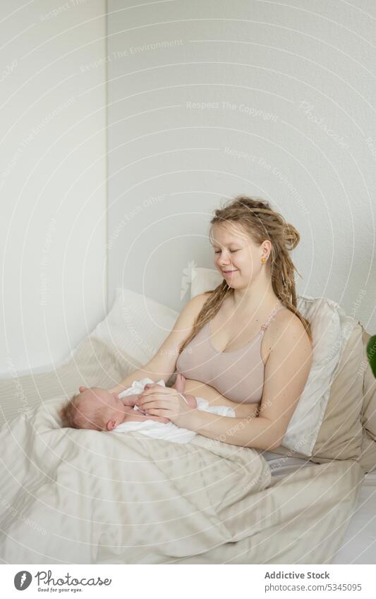 Mom sitting on bed with baby woman mother infant newborn mom childcare maternal cozy female comfort innocent motherhood together bedsheet lady peaceful delicate