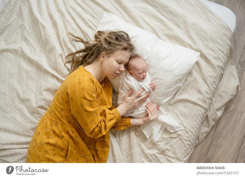 Woman sleeping on bed with baby woman mother infant newborn mom comfort cozy hug female child innocent vulnerable peaceful lying asleep embrace bedsheet