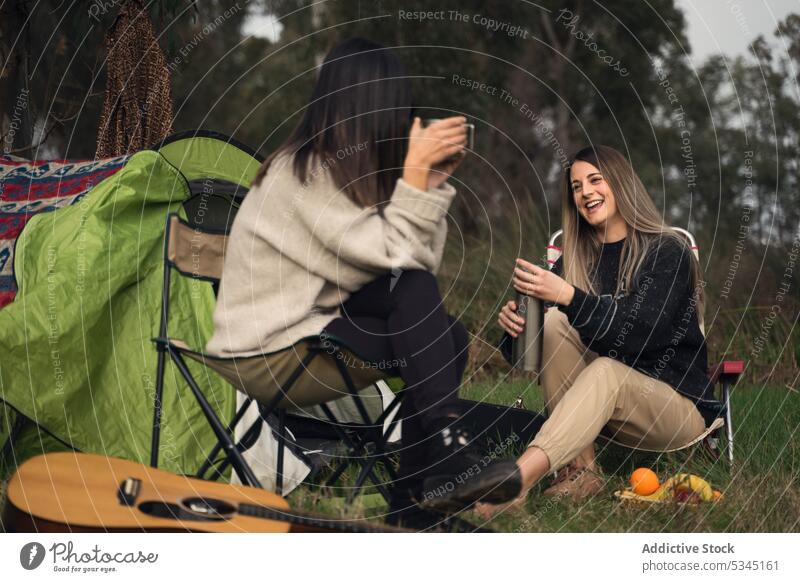 Women friends sitting in camp chairs in woods women campsite picnic forest talk tent smile weekend young female cheerful summer friendship glad camper vacation