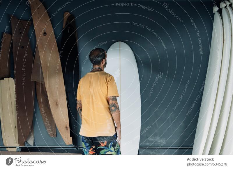 Unrecognizable man examining surfboard in workshop master examine check professional mechanic tool occupation male craftsman job artisan tattoo workman casual
