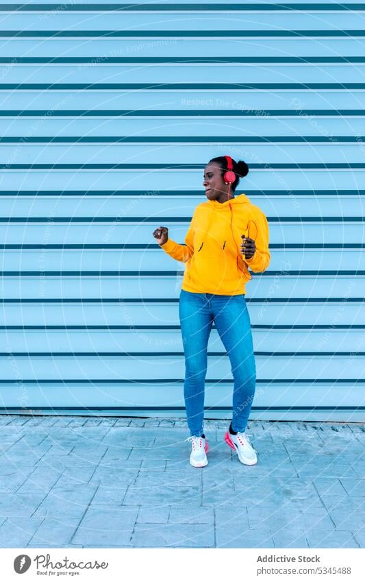 Stylish young lady in headphones dancing on street listen city casual style music smartphone woman wall female device african american song urban ethnic modern