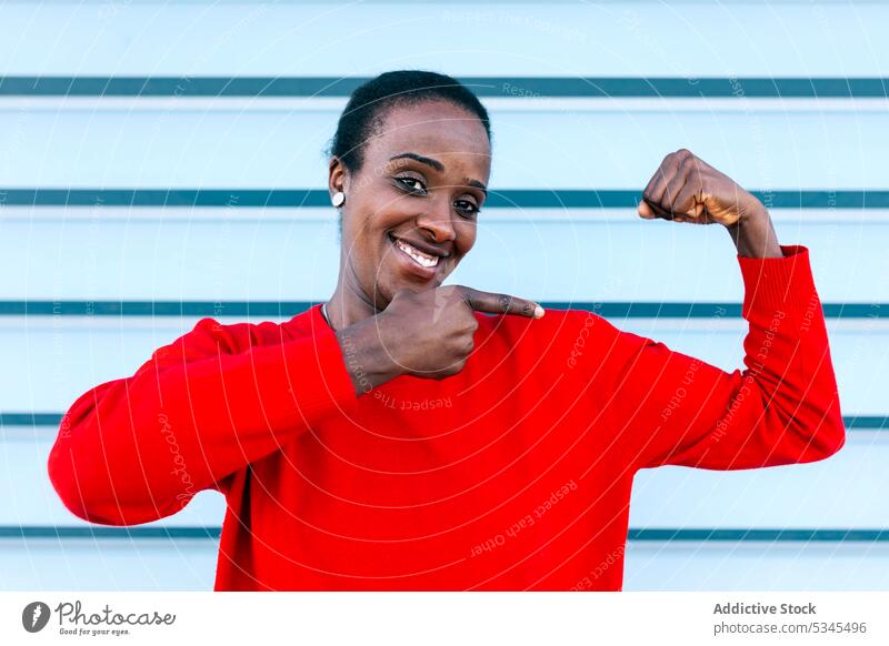 Delighted woman showing muscles on street bicep point smile content portrait female black african american fit strong demonstrate gesture expressive
