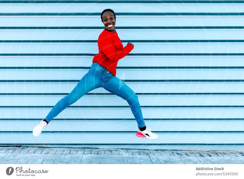 Joyful woman jumping on sidewalk model leap smile excited joy city street female black african american energy dynamic move active sportive style casual