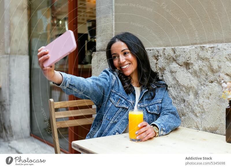 Cheerful ethnic woman taking selfie at table smartphone cafe juice street smile using positive moment happy young mobile female hispanic gadget device