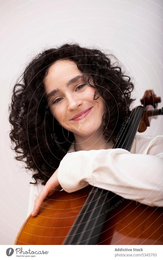 Happy woman with cello in music studio musician instrument portrait smile calm happy glad skill melody female curly hair delight hobby sit confident concentrate