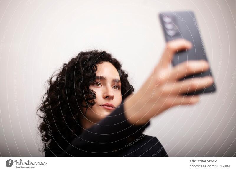 Unemotional woman taking selfie indoors smartphone sofa portrait mobile female device self portrait room using gadget curly hair serious formal couch cellphone