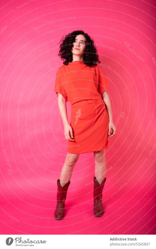 Stylish woman in red dress standing on pink background in studio confident model fashion outfit boot slim vogue trendy feminine young apparel style appearance