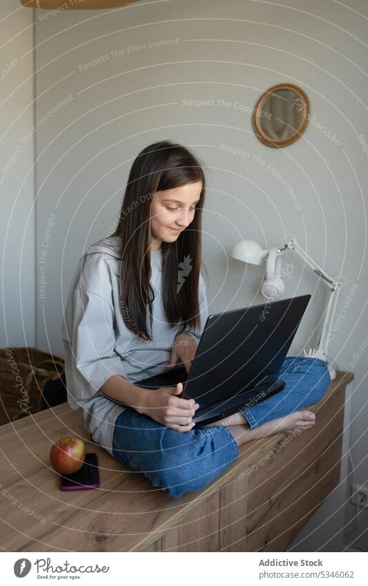 Smiling teenage girl with laptop sitting on table at home student desk apple snack content using study education browsing homework long hair knowledge device