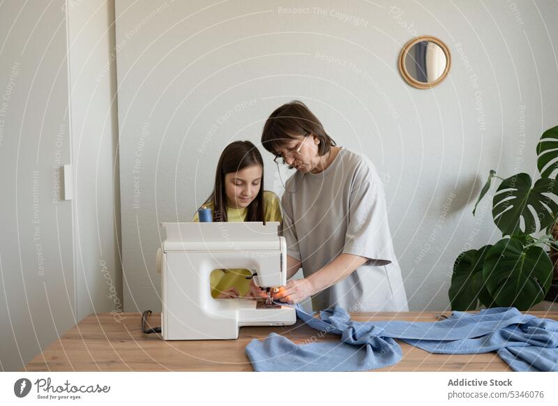 Concentrated woman sewing on machine with girl mother daughter teach dress craft together seamstress explain workshop occupation atelier professional