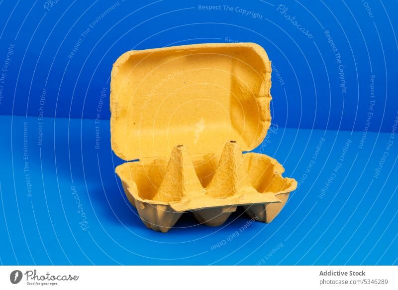 Generative AI illustration of empty yellow opened carton egg container placed on bright blue background representing concept of recycling packaging box package