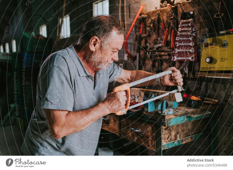 Elderly man cutting wooden plank with hand saw workshop workbench detail senior garage male tool old metal vise carpenter equipment aged woodwork woodworker