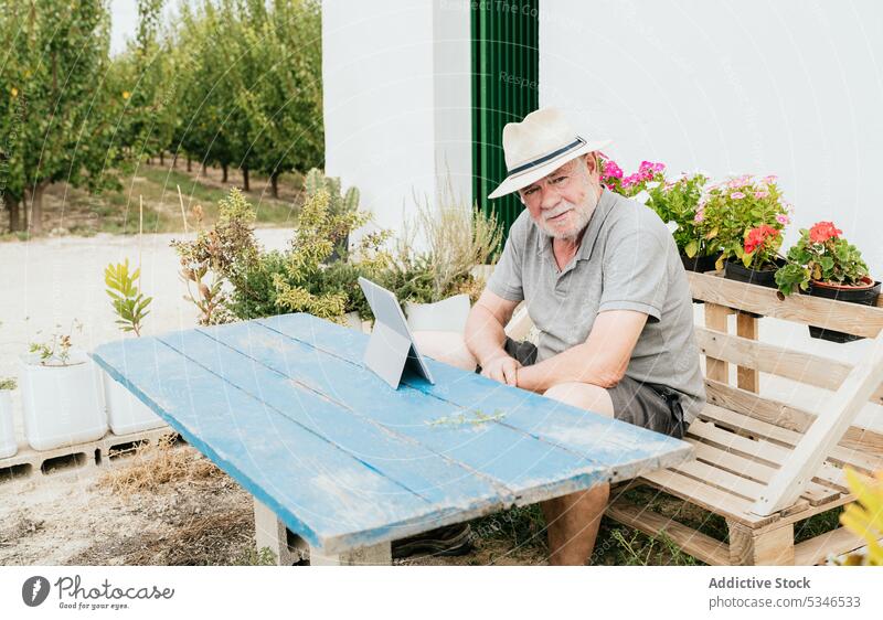 Aged farmer using tablet in garden man break house data countryside summer male bench shabby rest device gadget job sit casual digital elderly senior aged