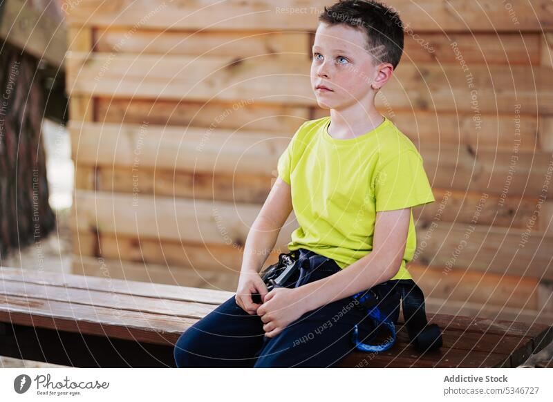Calm boy with trekking belt in wooden house pensive calm wait park thoughtful rope concentrate bench child serious kid summer casual sit schoolboy bright