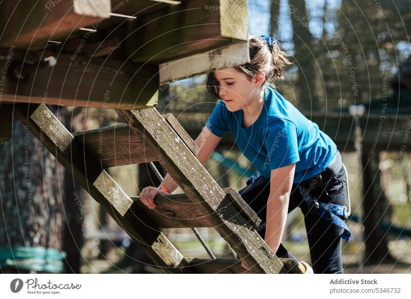 Focused girl climbing up wooden stairs in park rope platform activity kid summer concentrate child sun casual active daytime preteen walk adventure equipment
