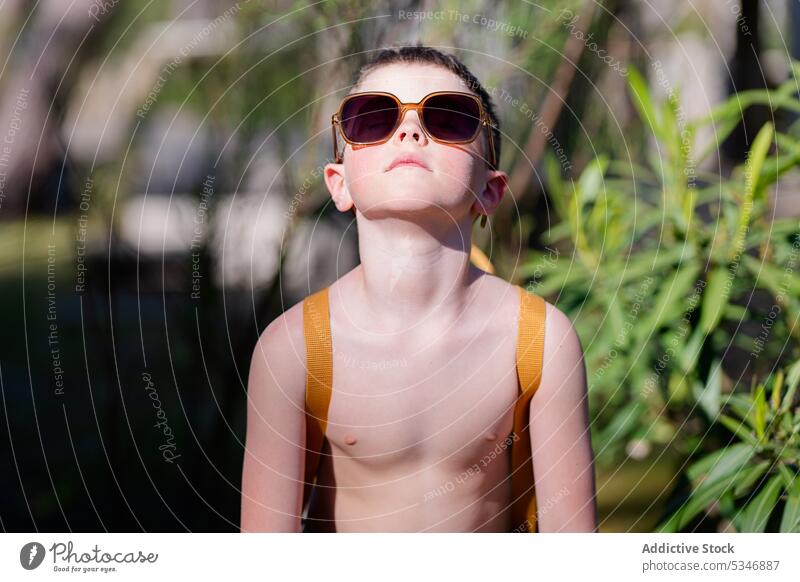 Stylish boy in sunglasses standing near plants nature summer vacation confident child garden eyewear naked torso green calm young fashion positive park alone