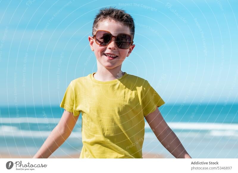 Boy with outstretched arms enjoying wind on beach boy sea water freedom blue sky child vacation happy sun glad childhood positive optimist sunglasses sunlight