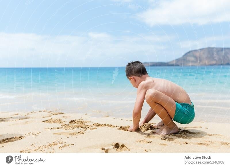 Unrecognizable boy in shorts playing with sand beach sea kid shore activity season carefree pleasure seaside resort child water coast relax weekend ocean sit