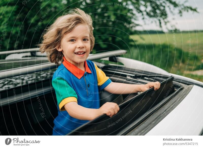 Adorable happy little boy stands in open car sunroof during trip at summer. kid travel child family people vehicle young carefree freedom journey cheerful
