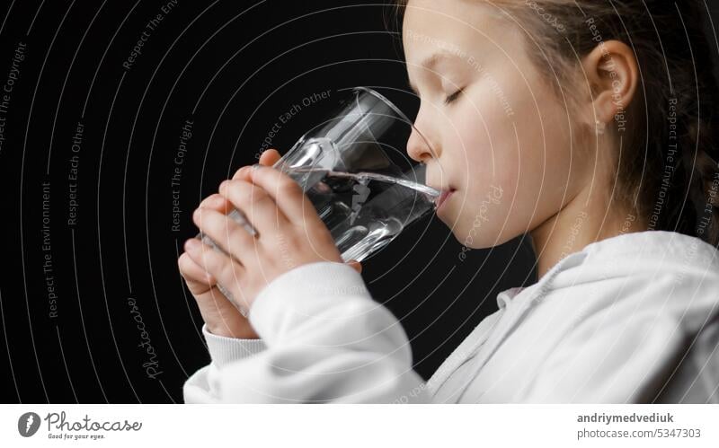 Water balance and children health care. Little girl drinks fresh transparent pure filtered mineral water at home. Thirsty dehydrated teenager holds glass hydrating thirst in the morning to be healthy