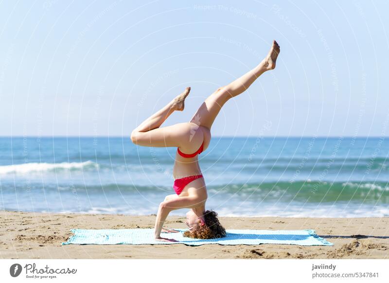 Flexible woman in bikini doing yoga in beach stretch coast seashore healthy nature ocean tripod headstand slim sunlight summer slender bright practice fit