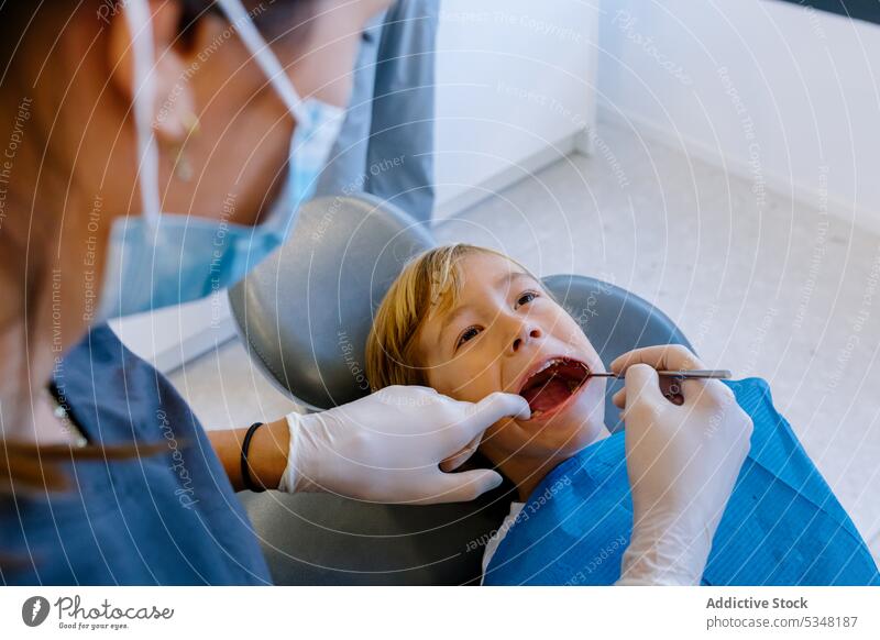 Anonymous dentist treating teeth of patient woman examine medicine child kid uniform doctor mask health care tool work specialist professional dental dentistry