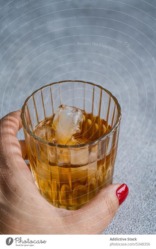 Glass of drink with ice alcohol beverage cognac cola cold crystal cube dinner glass hand hold red rest strong table vodka woman crop anonymous unrecognizable