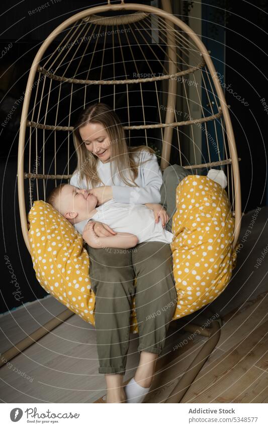 Woman with boy relaxing on hanging chair in house mother son wicker together smile leisure comfort rest happy weekend casual lounge kid friend carefree
