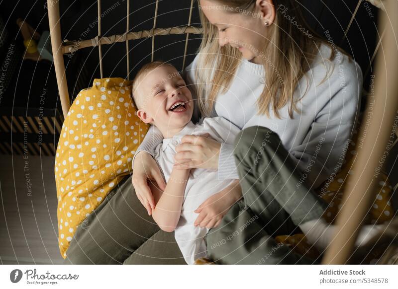 Woman with boy relaxing on hanging chair in house mother son wicker together smile leisure comfort rest happy weekend casual lounge kid friend carefree