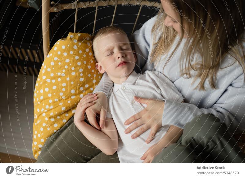 Mother with sleeping son in hanging chair mother relax rest love care woman together bonding nap kid boy comfort casual asleep calm sit lap motherhood parent