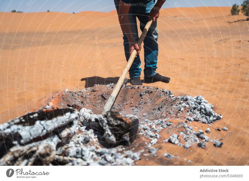 Cropped man preparing hot charcoal to cook in desert ground sand prepare bonfire shovel smoke marrakesh morocco burn heat nature dry soil tool process organic