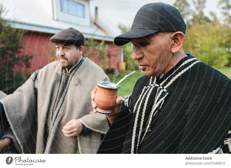 Senior friends in woolen ponchos sharing hot tea in park men yerba mate mapuche spend time together grass drink friendship tradition lawn meadow grassy temuco