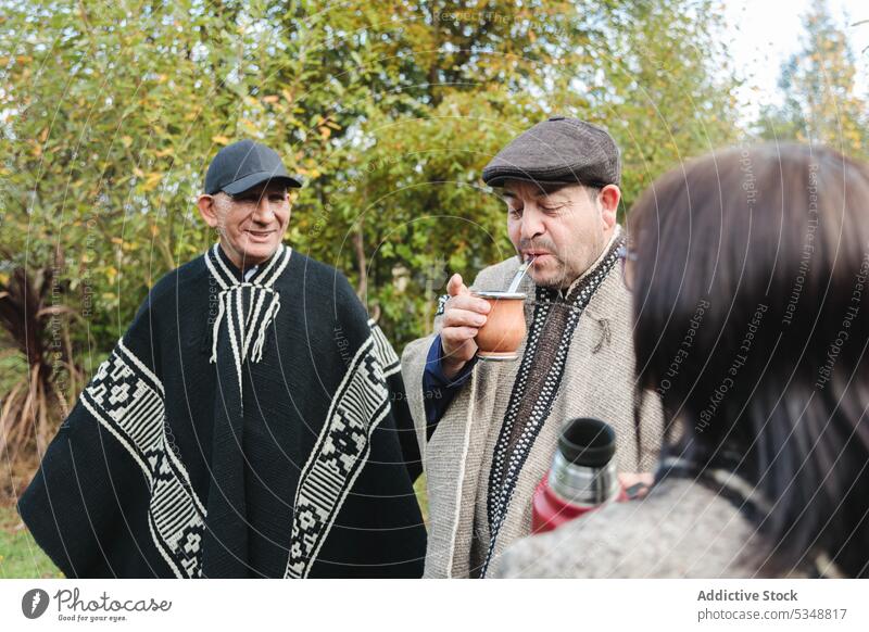 Smiling senior friends with drinks in park together men woman yerba mate mapuche spend time thermos grass friendship tradition lawn meadow grassy temuco chile