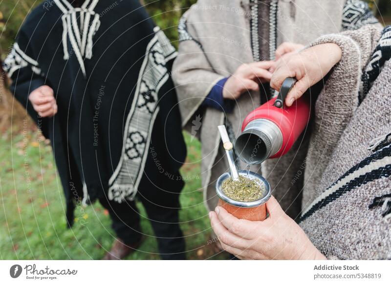 Cropped people in woolen ponchos sharing hot tea in park friend drink together yerba mate hot drink gather spend time thermos mapuche friendship cup casual