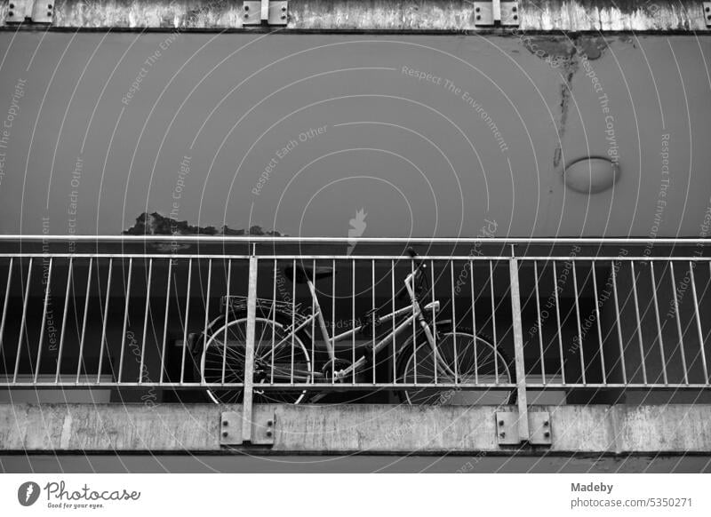 Bicycle on the balcony of a dilapidated gray apartment building and tenement with railings in the Masthildenviertel district of Offenbach am Main in Hesse in neo-realistic black and white