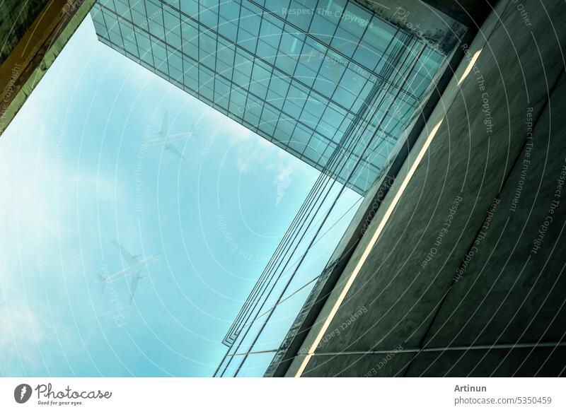 Bottom up view of modern sustainable glass office building and airplane flying in blue sky. Exterior view of corporate headquarters glass building architecture. Energy-efficient building. Glass window