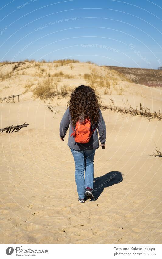 Long-haired curly-haired woman with a backpack walking on sand dunes Woman Adult Backpack Lithuania Neringa Gray Dunes Dead Dunes sandy Curonian Spit lithuanian