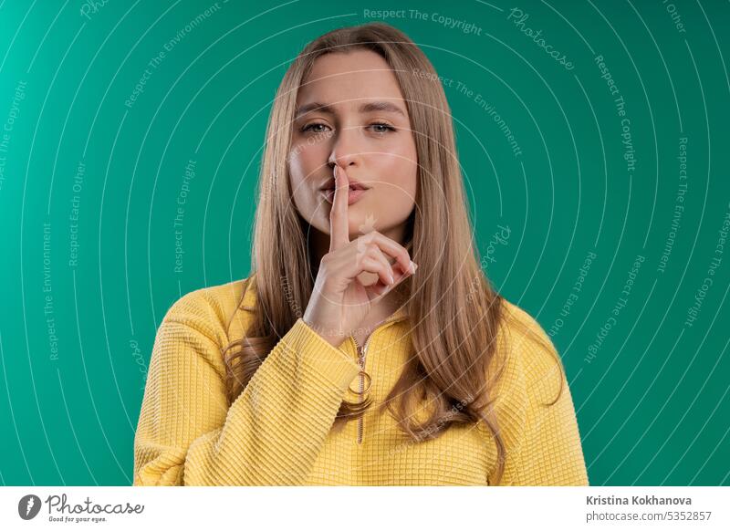 Smiling pretty woman with finger on lips - shhh, secret, silence, blue studio asking background biting charming closeup concept conspiracy contemplation cute