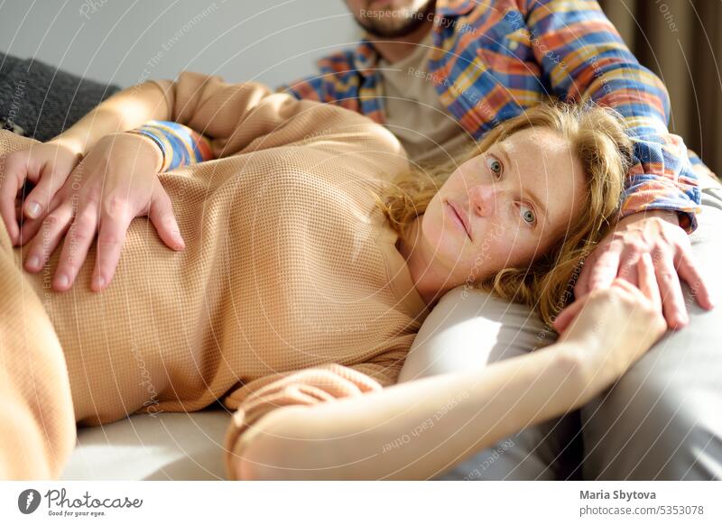 Young beautiful pregnant woman is lying on her husband's lap. Happy young couple relaxing on the couch at home. tender happy parents-to-be mom-to-be future